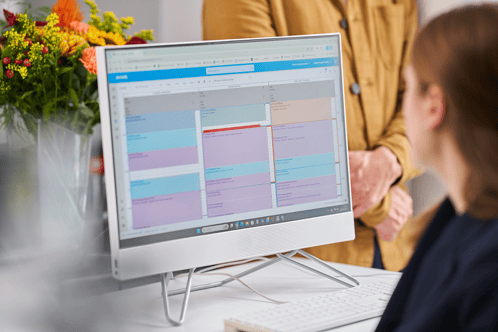A photograph of a receptionist looking at a computer with the Dentally software on screen displaying a calendar